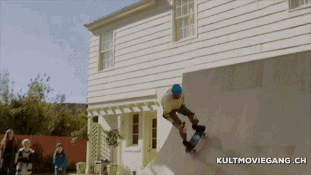 a man is riding a skateboard down a ramp in front of a house with kultmoviegang.ch written below him