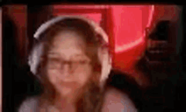 a woman wearing headphones and glasses is sitting in front of a red wall .