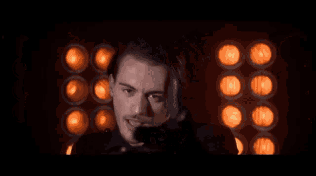 a man with a mustache is smoking a cigarette in front of a wall of lights