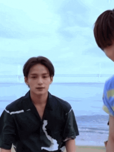 a man in a black shirt is standing on a beach talking to another man in a blue shirt .