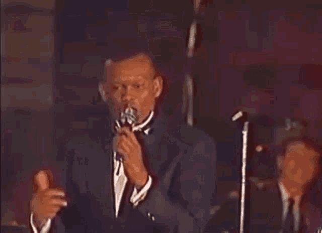 a man in a tuxedo and bow tie stands in front of a microphone