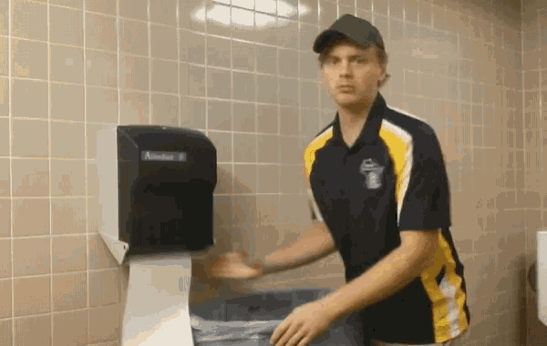 a man wearing a black and yellow shirt with the number 1 on it is standing in front of a kleenex dispenser
