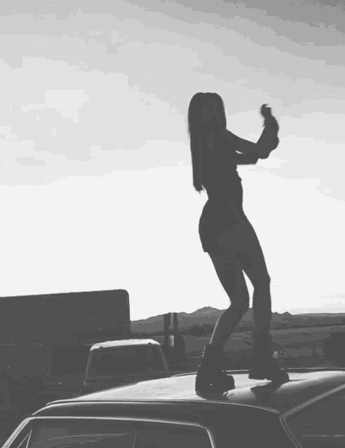 a black and white photo of a woman standing on top of a car