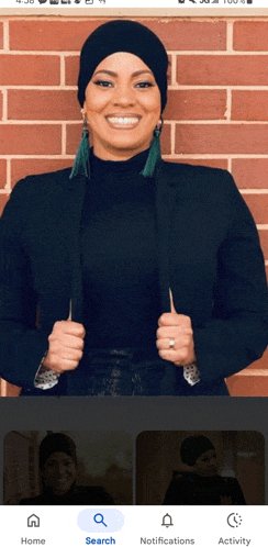 a woman wearing a black hat and earrings is smiling in front of a brick wall ..