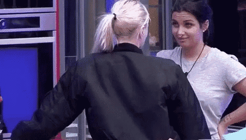 two women are standing next to each other in a kitchen . one of the women is wearing a black jacket .