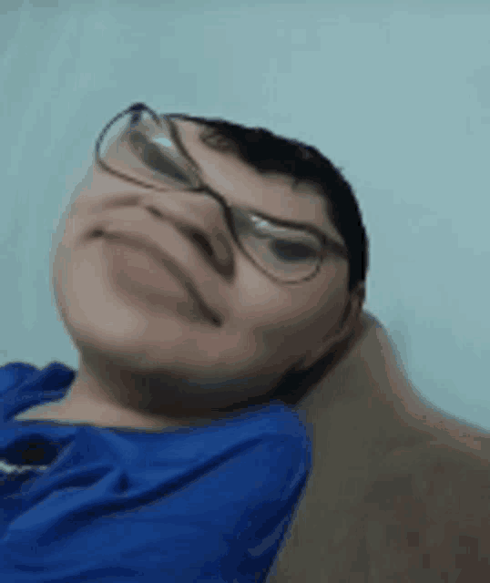 a young boy wearing glasses and a blue shirt is making a funny face .
