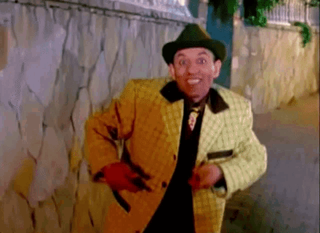 a man in a yellow jacket and green hat is walking down a street .