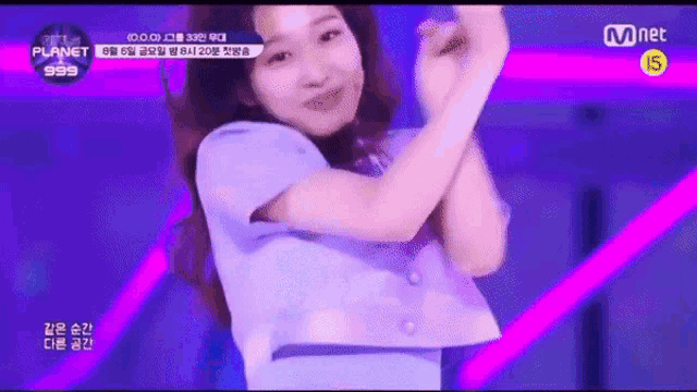 a woman in a blue shirt is dancing on a stage with a mnet logo in the background .