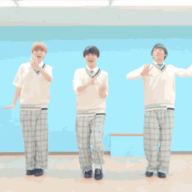 three young men in school uniforms are dancing together