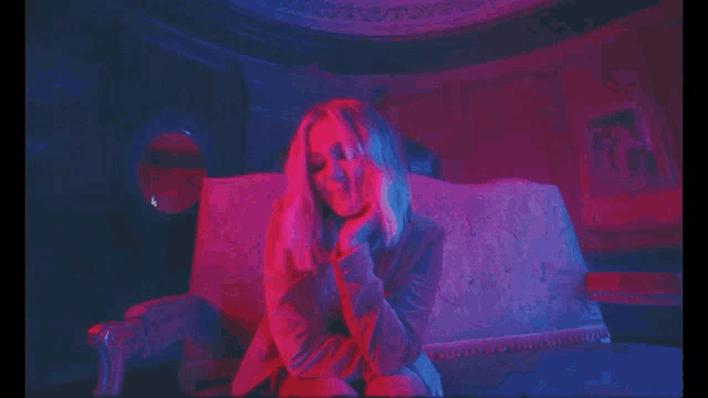 a woman is sitting on a couch in a dark room with red and blue lights behind her