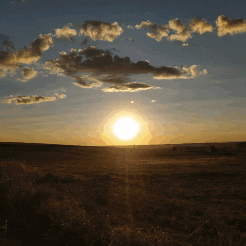 the sun is setting over a field with clouds