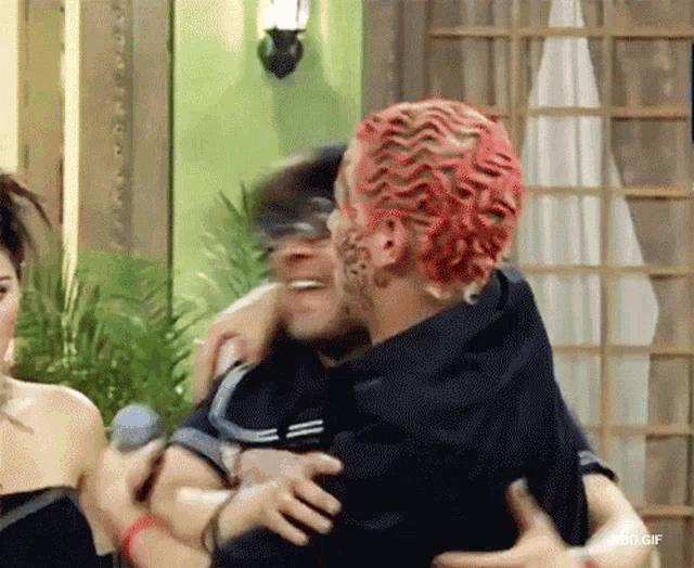 a man with red hair is hugging another man in a room ..