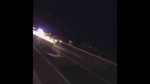 a car is driving down a highway at night and there is a light in the sky .
