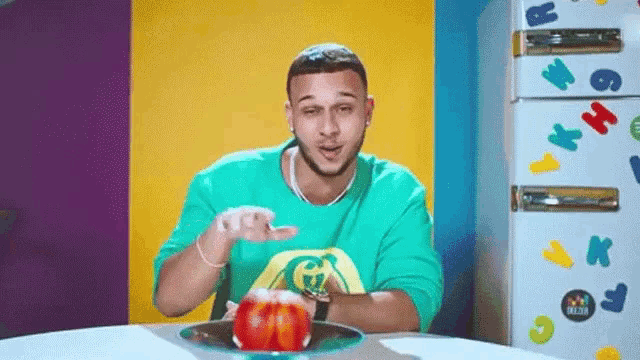 a man is sitting at a table with a plate of food in front of a refrigerator with letters on it