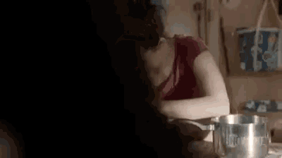 a woman in a red shirt is sitting at a table with a pot on it .