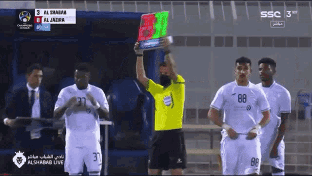a group of soccer players standing in front of a referee holding a sign that says 3 alshabab