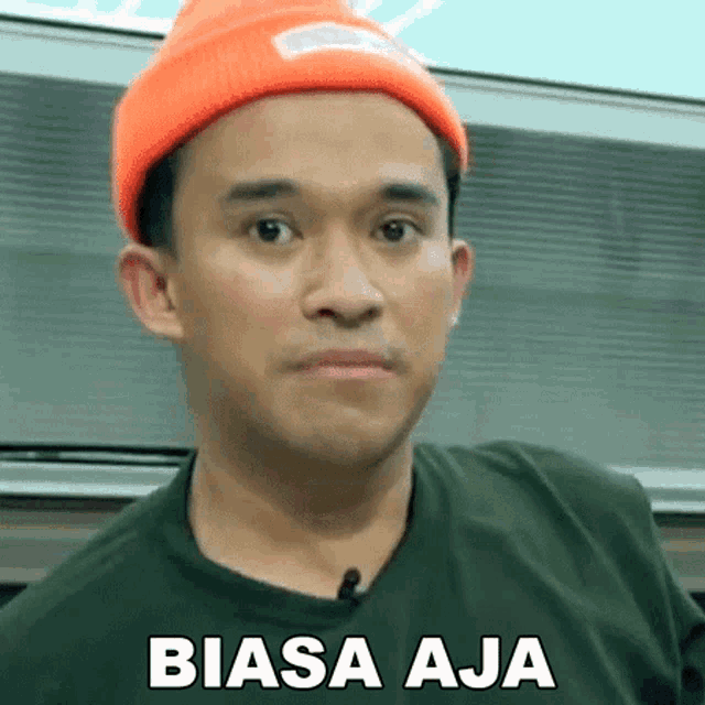 a man wearing an orange beanie and a green shirt has the word biasa aja written on his face