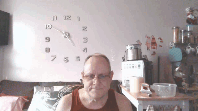 a man sitting in front of a wall clock that shows the time as 10:11