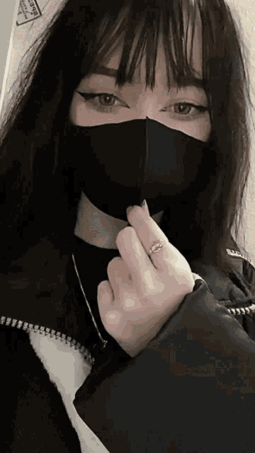a girl wearing a black mask and a ring on her finger is making a heart shape with her hand