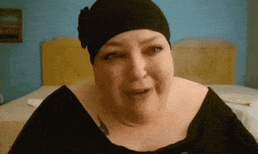 a woman wearing a black hat is sitting in front of a yellow headboard