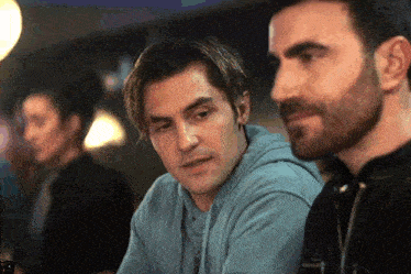 a man with a beard is sitting next to another man in a bar .