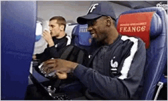 a man in a baseball cap is using a laptop on an airplane seat that says france