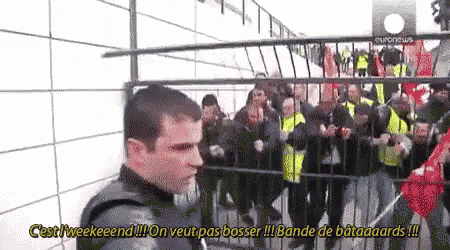 a man is standing in front of a crowd of people behind a fence and says " c'est l' weekend "
