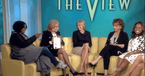 a group of women sitting on a couch in front of a sign that says the view
