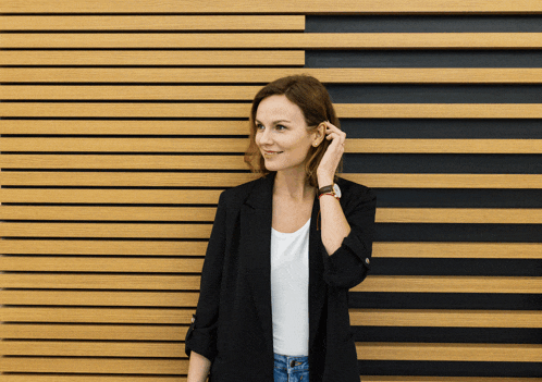 a woman in a black jacket stands in front of a wood paneled wall