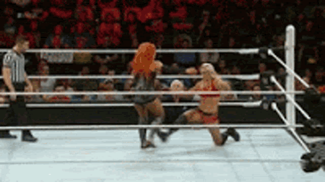 two women are wrestling in a ring with a referee in the background