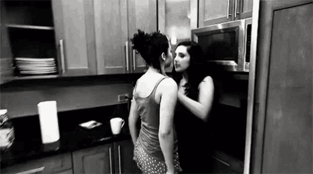 a couple of women are kissing in a kitchen .