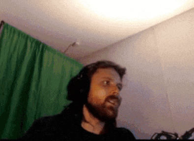 a man with a beard wearing headphones is standing in front of a green curtain
