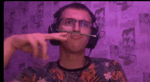 a man wearing headphones and glasses is holding a pencil to his mouth .