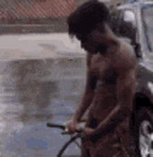 a shirtless man is holding a hose in a puddle of water .