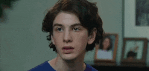 a close up of a young man 's face in a living room with pictures in the background .