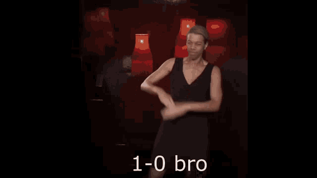 a woman in a black dress is dancing in front of red lamps with the words 1-0 bro written below her .