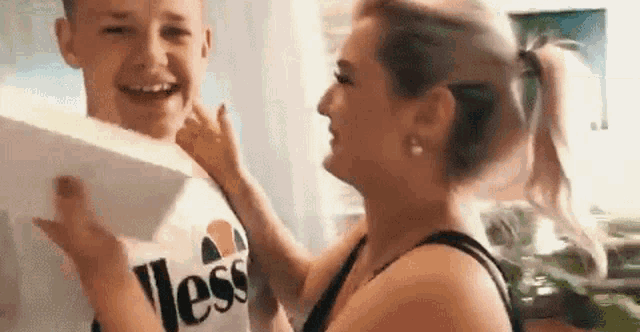 a woman is putting a box on a boy 's shoulder and the boy is smiling .