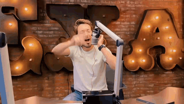 a man is singing into a microphone in front of a brick wall with the letter a on it