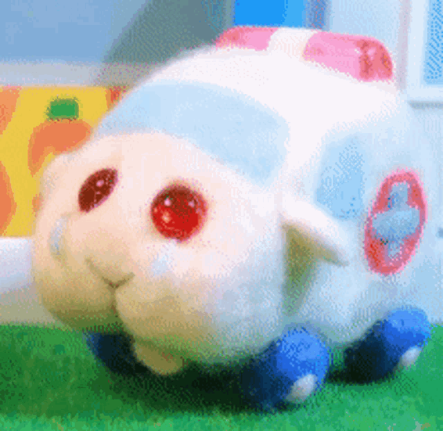 a white stuffed animal with red eyes and a cross on the back is sitting on the grass .