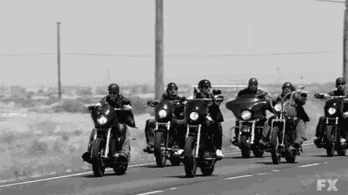a group of men are riding motorcycles down a road in a black and white photo .