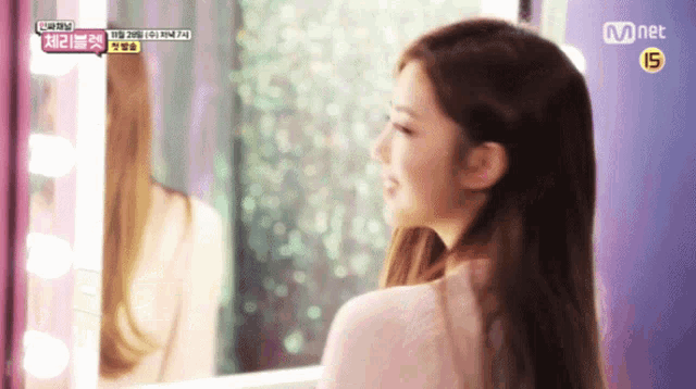 a woman is looking at herself in a mirror with mnet written on the bottom right
