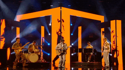 a group of men are playing instruments on a stage in front of orange lights