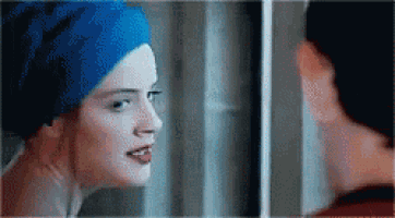 a woman with a blue towel on her head is looking at herself in the mirror .