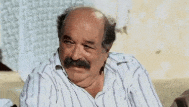 a bald man with a mustache and a striped shirt is sitting on a couch .