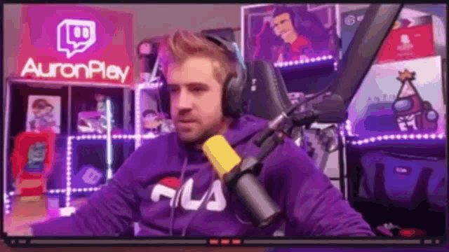 a man in a purple hoodie is sitting in front of a microphone in a room .
