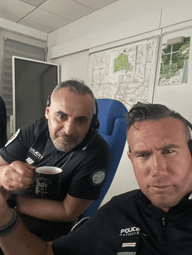 two police officers sitting next to each other with one holding a cup of coffee