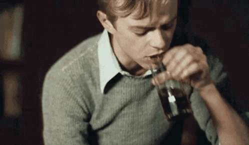 a young man in a sweater is drinking from a glass through a straw .