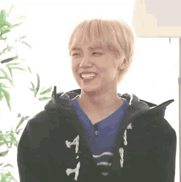 a young man with blonde hair is wearing a blue shirt and a black jacket .