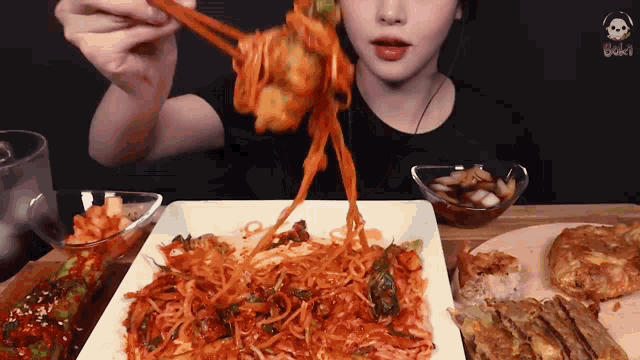 a woman is eating noodles with chopsticks from a plate of food