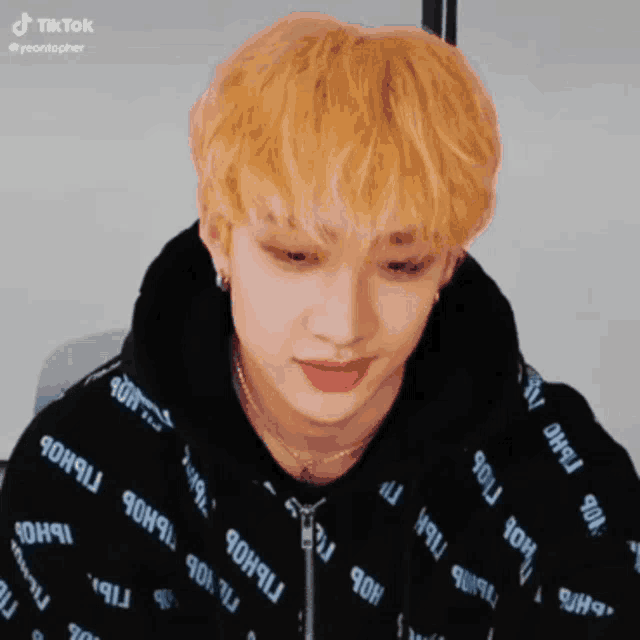 a young man with blonde hair is wearing a black hoodie with a pattern on it .